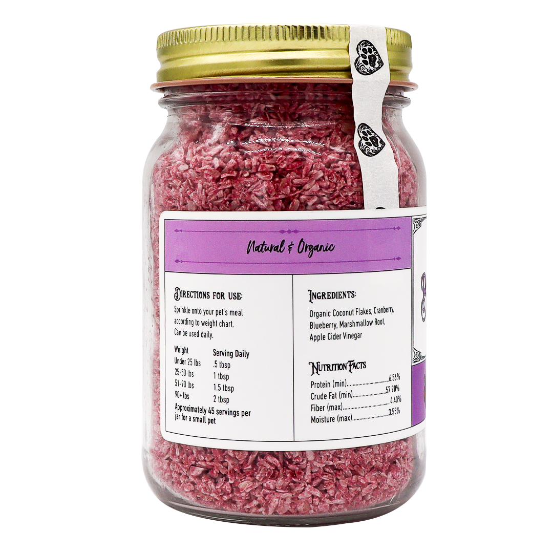 A glass jar with a gold lid holds Project Sudz | Berry Boost Urinary Support for Dogs and Cats – 210g, featuring pink shredded coconut flakes infused with cranberry. The mostly white and purple label highlights a natural, organic theme and includes ingredients, nutritional facts, serving sizes, and pet-use directions.