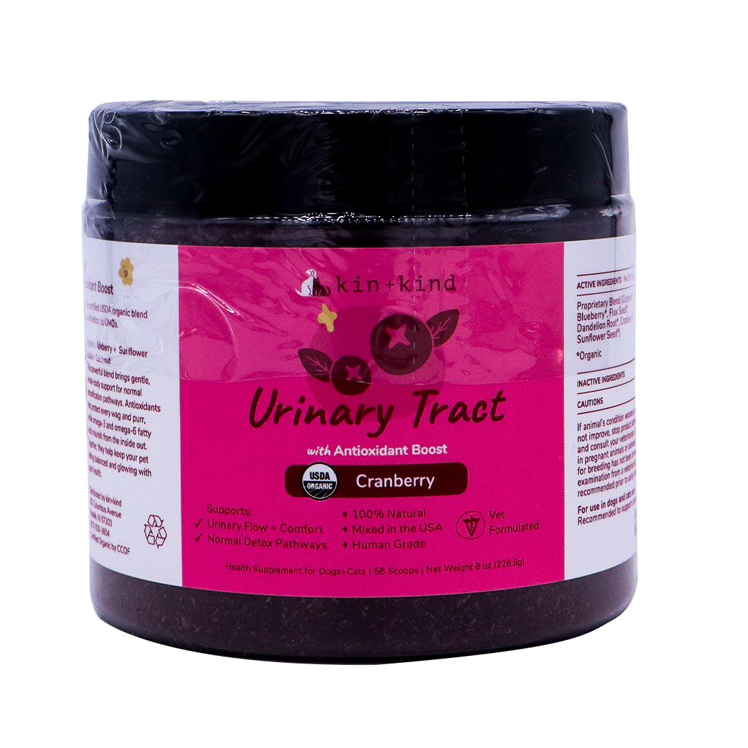 A jar of kin+kind Urinary Tract with Antioxidant Boost supplement for pets, featuring a cranberry flavor, comes in a pink and white label that displays its USDA organic certification and emphasizes its benefits for both dogs and cats. Vet-formulated, this top-tier organic pet supplement is designed to support optimal urinary tract health for your furry companions.