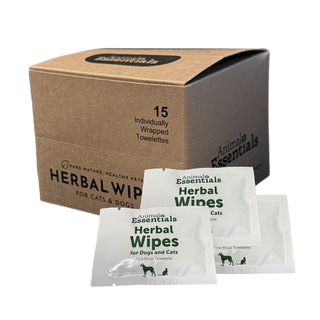 A brown box labeled Animal Essentials | Herbal Wipes (15 count box) sits with three individual white towelette packets displayed in front. Designed for natural grooming, the box notes it contains 15 individually wrapped herbal pet wipes for cats and dogs.