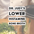 A chef in white stands beside a slow cooker with chopped green herbs and vegetables on a wooden surface. Text reads: Dr. Judy's Lower Histamine Bone Broth Recipe—an ideal, nutrient-rich choice for those seeking a delicious option. Download your free PDF of Dr. Judy's Lower Histamine Bone Broth Recipe today!.