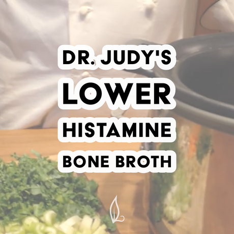 A chef in white stands beside a slow cooker with chopped green herbs and vegetables on a wooden surface. Text reads: Dr. Judy's Lower Histamine Bone Broth Recipe—an ideal, nutrient-rich choice for those seeking a delicious option. Download your free PDF of Dr. Judy's Lower Histamine Bone Broth Recipe today!.