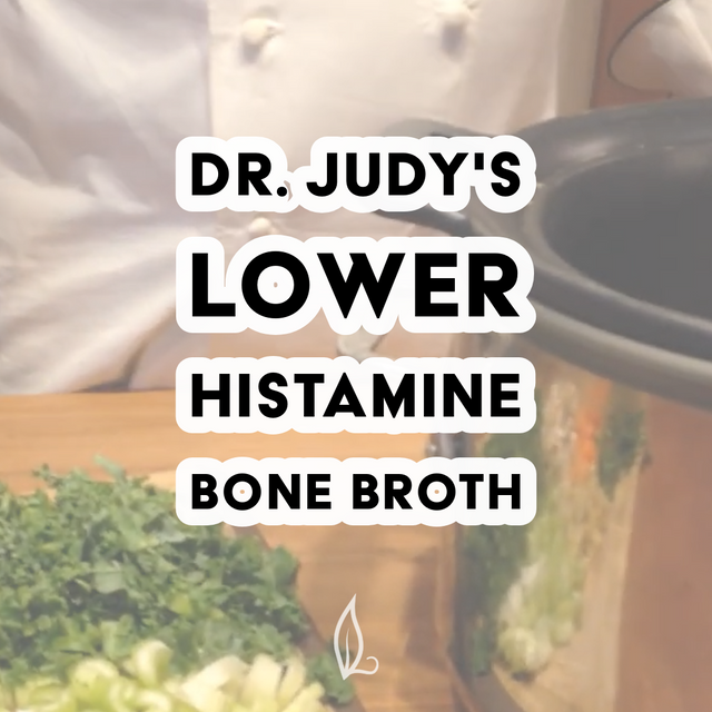 A chef in white stands beside a slow cooker with chopped green herbs and vegetables on a wooden surface. Text reads: Dr. Judy's Lower Histamine Bone Broth Recipe—an ideal, nutrient-rich choice for those seeking a delicious option. Download your free PDF of Dr. Judy's Lower Histamine Bone Broth Recipe today!.