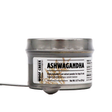 A small silver tin of Woof Creek | Ashwagandha Root Extract Powder for Dogs + Cats, labeled accordingly, contains root extract powder designed to provide natural stress relief for dogs and cats. A metal spoon filled with the powder is placed in front of the tin on a white background.