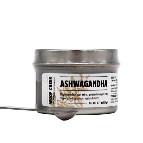 A small silver tin of Woof Creek | Ashwagandha Root Extract Powder for Dogs + Cats, labeled accordingly, contains root extract powder designed to provide natural stress relief for dogs and cats. A metal spoon filled with the powder is placed in front of the tin on a white background.