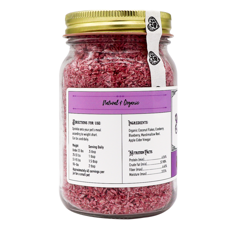 A glass jar with a gold lid holds Project Sudz | Berry Boost Urinary Support for Dogs and Cats – 210g, featuring pink shredded coconut flakes infused with cranberry. The mostly white and purple label highlights a natural, organic theme and includes ingredients, nutritional facts, serving sizes, and pet-use directions.
