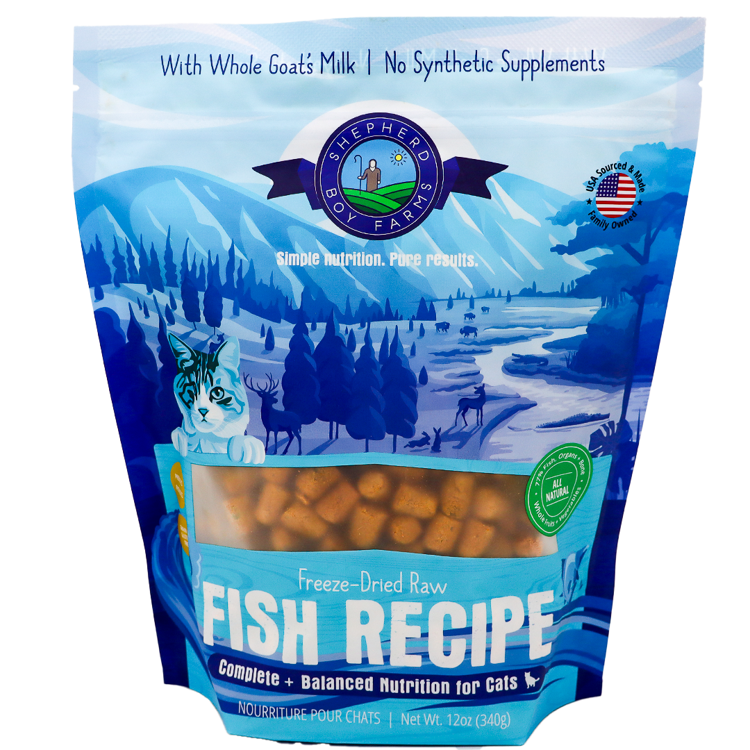 A blue and white 14oz bag of Shepherd Boy Farms | Fish Recipe for Cats displays mountains, trees, a cat illustration, and the product visible through a window. This grain-free cat food is made with goat’s milk and contains no synthetic supplements.