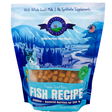 A blue and white 14oz bag of Shepherd Boy Farms | Fish Recipe for Cats displays mountains, trees, a cat illustration, and the product visible through a window. This grain-free cat food is made with goat’s milk and contains no synthetic supplements.
