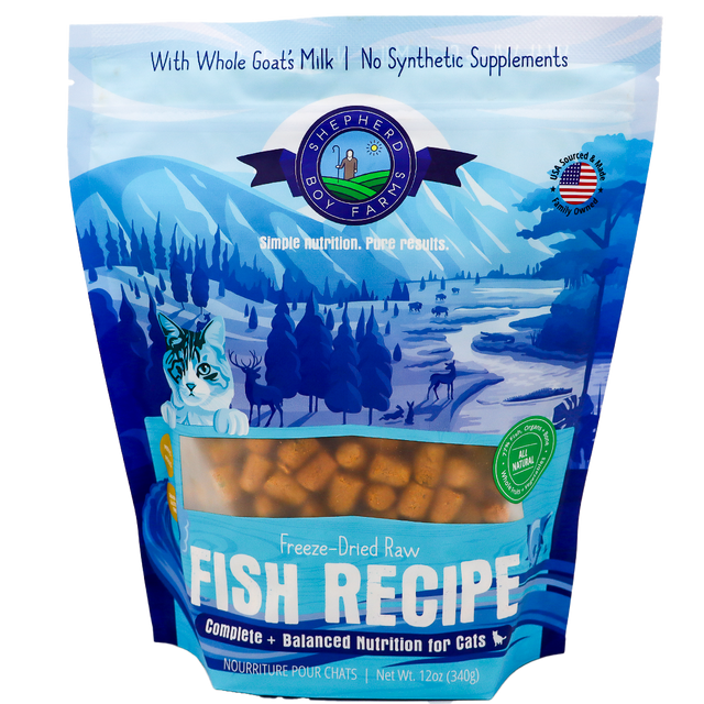 A blue and white 14oz bag of Shepherd Boy Farms | Fish Recipe for Cats displays mountains, trees, a cat illustration, and the product visible through a window. This grain-free cat food is made with goat’s milk and contains no synthetic supplements.