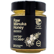 A glass jar of Center of Paradise | RAW MANUKA HONEY UMF 20+ MGO 850+ with a black label featuring the text UMF 20+ MGO 850+ and a botanical illustration of a flower branch.