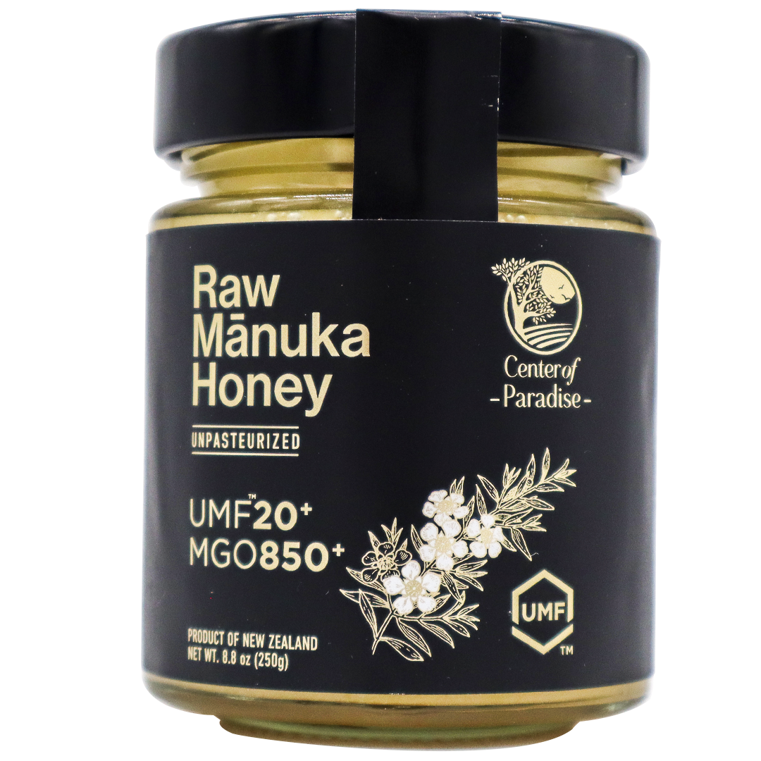 A glass jar of Center of Paradise | RAW MANUKA HONEY UMF 20+ MGO 850+ with a black label featuring the text UMF 20+ MGO 850+ and a botanical illustration of a flower branch.