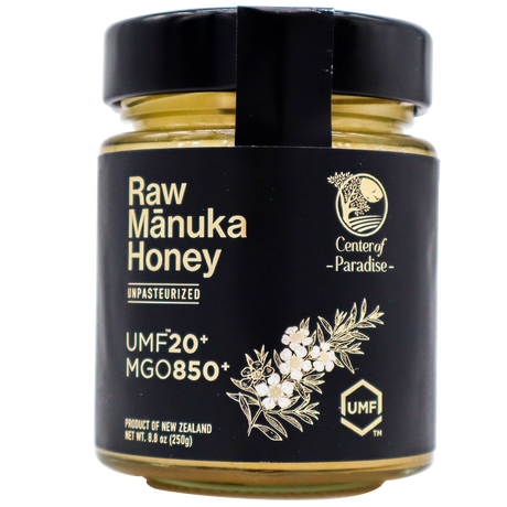 A glass jar of Center of Paradise | RAW MANUKA HONEY UMF 20+ MGO 850+ with a black label featuring the text UMF 20+ MGO 850+ and a botanical illustration of a flower branch.