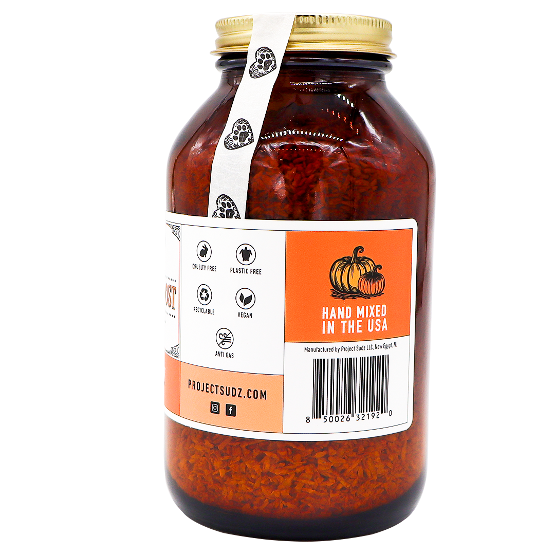 Project Sudz | Pumpkin Boost Digestive Health for Dogs and Cats - 210g comes in a large amber glass jar with a gold lid, containing dried orange contents designed to support your pet’s digestive health. The label displays icons for cruelty free, plastic free, moisture protection, and vegan. Next to a pumpkin illustration, text reads “Hand Mixed in the USA”—highlighting a blend of slippery elm and soil-based probiotics carefully crafted for your pet’s well-being.
